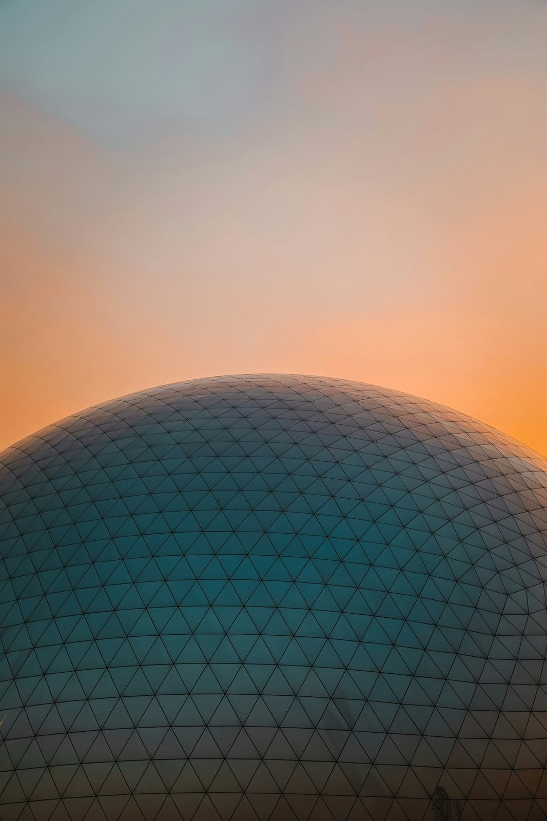 Geodesic glass dome against an orange sunset sky