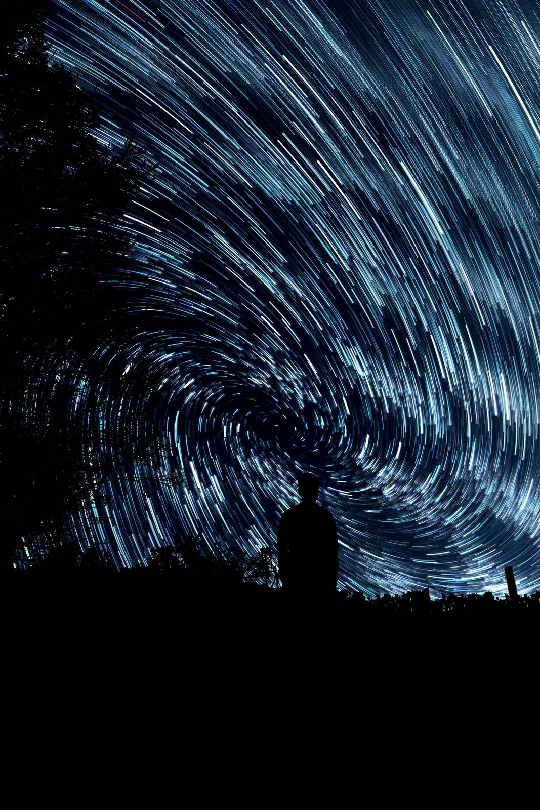 Person silhouetted under swirling star trails in the night sky
