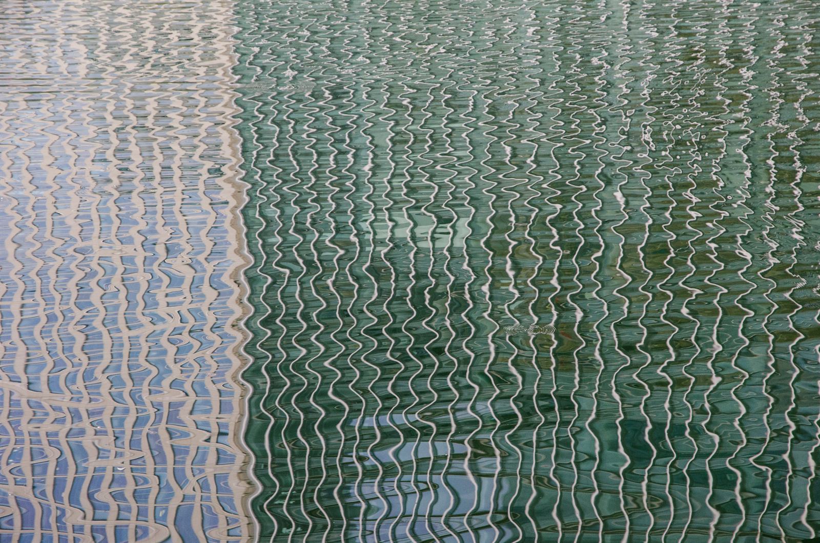Building reflected in rippling green-blue water